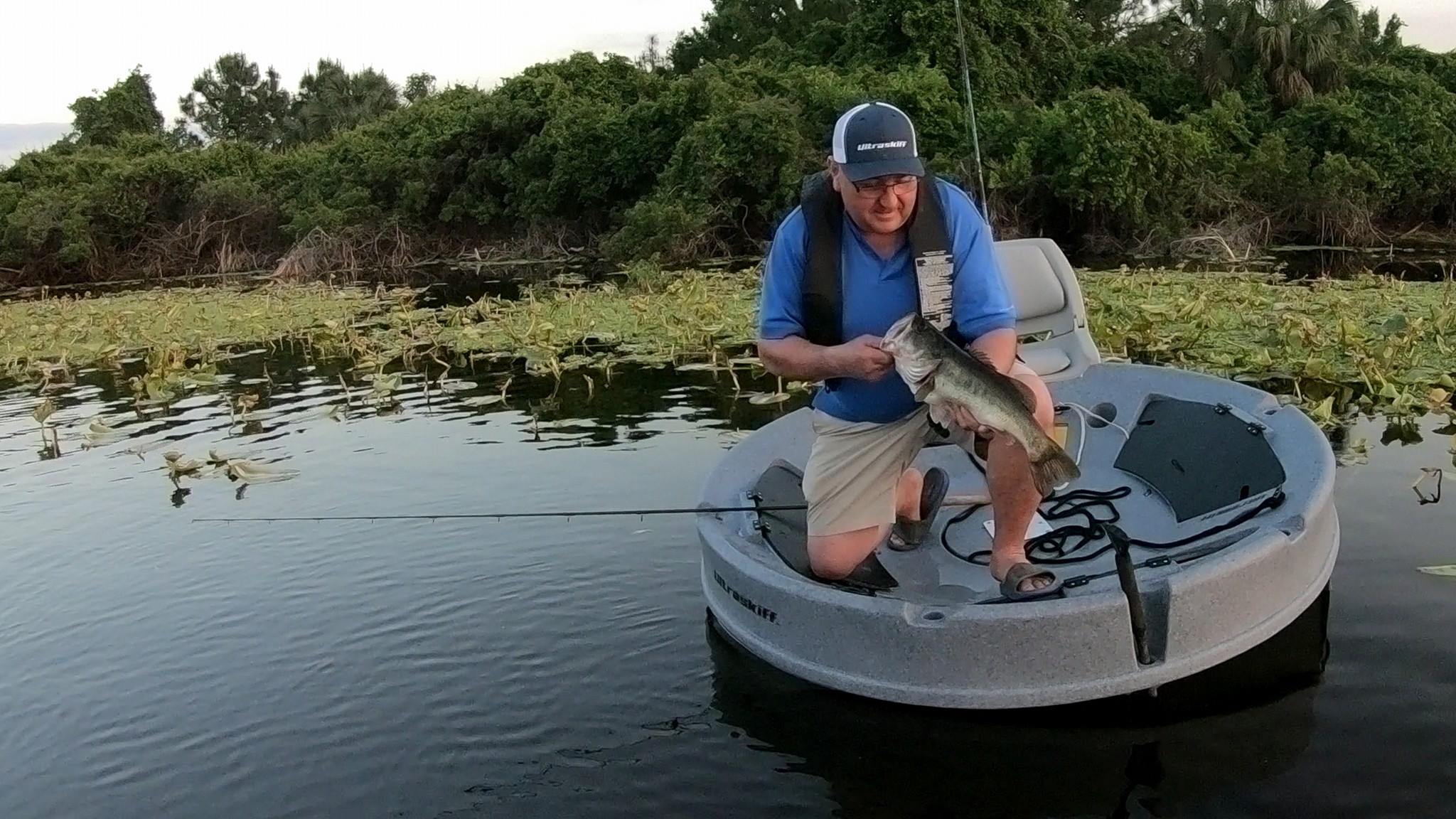 Man on a small boat holding a fish with a natural water and greenery background