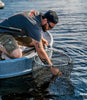 Man on Edge of Ultraskiff Netting a Fish